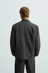 Blazer negro de corte relajado con cuello de solapa de muesca desmontable, manga larga, bolsillos frontales ocultos y cierre frontal con botones.