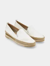 Zapato tipo slip-on de color blanco con elásticos laterales para facilitar el calce. Presenta una suela de plataforma con detalle de yute trenzado en el contorno y base de goma en tonos beige.