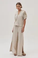 Blusa de lino color arena, de manga corta, con cuello redondo y lazo ajustable. Presenta bordados en las mangas y el escote.