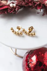 Par de aros dorados con forma curva y cinco bolitas de acero quirúrgico en cada aro.