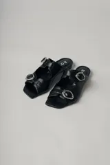 Sandalias planas de cuero color marrón con dos tiras anchas sobre el empeine, cada una con hebilla dorada.