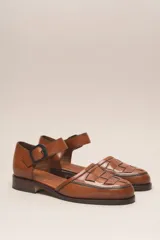 Zapato marrón de cuero con correa al tobillo y hebilla negra. Diseño trenzado en la parte delantera.