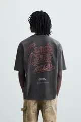 Camiseta negra de corte holgado con cuello redondo y mangas cortas. Estampado frontal con una ilustración de una mujer en un cohete y la leyenda "Cherry Pilot Blush Delight".