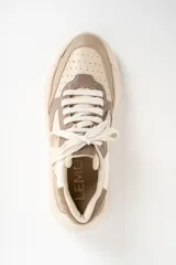 Zapatilla urbana de mujer con plataforma gruesa, combinando paneles de cuero en tonos beige, blanco roto y marrón topo. Presenta cordones anchos y un detalle de texto en el talón.