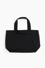 Bolso shopper grande de lona color negro, con doble asa de mano y detalle bordado tono sobre tono en un lateral.