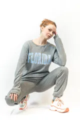 Sweater gris de corte clásico con cuello redondo y puños y cintura acanalados. Estampado frontal con la palabra "Florida" en letras celestes con borde blanco.