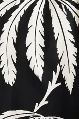 Vestido corto evasé de algodón con estampado de hojas color blanco sobre fondo negro. Tiene mangas globo cortas de diseño raglán y escote redondo con cordón para ajustar.