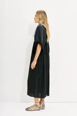 Vestido midi negro de calce amplio y mangas al codo. Tiene apliques de gasa en escote y mangas, y recortes con frunce en la cintura.