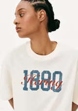 Camiseta beige de corte amplio con estampa frontal con el texto "1880 Hering" en azul y rojo.