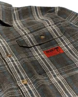 Camisa de franela a cuadros en tonos beige, gris y negro. Tiene cuello clásico, cierre con botones, dos bolsillos con solapa en el pecho y puños abotonados.