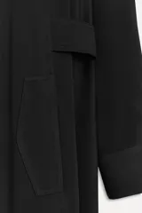 Vestido largo negro tipo camisero, confeccionado en viscosa. Tiene cuello solapa, manga larga con puños, bolsillos delanteros y cierre frontal con botones. Incluye cinturón ajustable con trabillas y botones.