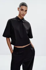 Camisa negra de popelín con cuello solapa y manga ancha por debajo del codo. Detalle de pinzas en la espalda y cierre frontal con botones ocultos por solapa.