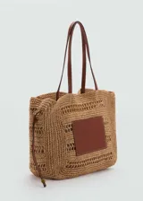Bolso tipo shopper de fibra natural color beige, con doble asa de mano de cuero marrón y cierre regulable con botón magnético.