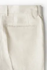 Pantalón de traje de lino color beige, corte slim fit, con cierre y corchete oculto, bolsillos laterales y traseros ribeteados.
