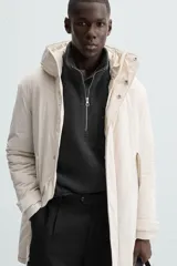 Parka color crudo de tejido técnico acolchado, con cuello alto y capucha ajustable. Tiene mangas largas con puños ajustables, bolsillos frontales con solapa, bolsillo interior y cierre frontal con cremallera oculta por solapa con botones a presión.