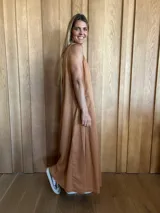 Vestido largo color crudo, sin mangas y con escote en V. Presenta aberturas laterales en el ruedo y bolsillos laterales a la altura de la cadera.