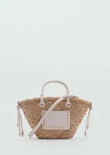 Bolso tipo canasta de paja trenzada color beige, con asas cortas y correa larga desmontable de cuero sintético color crema. Tiene un bolsillo exterior con apliques de tachas doradas.