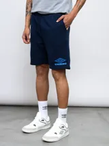 Bermuda deportiva azul marino de felpa sin friza, con cintura elástica ajustable con cordón, bolsillos laterales y logo de Umbro bordado en azul en la pierna izquierda.
