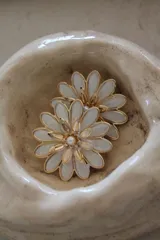 Par de aros con forma de flor, con pétalos blancos y centro dorado con una perla.