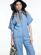 Camisa celeste de manga corta confeccionada en denim liviano de tencel. Tiene calce cuadrado y relajado, cierre frontal con tapeta escondida y costuras en color contraste.