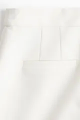 Short de vestir color blanco, de tiro alto, con bolsillos al bies y bolsillos insertados decorativos atrás. Presenta cierre frontal con botón.