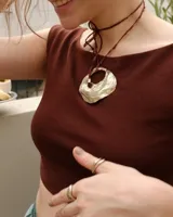 Collar con dije dorado en forma de concha marina y cordón marrón de seda natural.