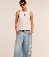 Pantalón de jeans celeste de corte amplio, con cintura con trabillas, cierre tradicional y bolsillos. Presenta estampa lateral estilo maorí en color blanco.