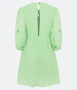 Vestido corto color verde lima con estampado de flores en verde claro, escote en V con lazo, mangas 3/4 con puños elásticos y falda con volantes.