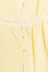 Blusa amarilla sin mangas con escote en pico y detalle de puntillas blancas. Cierre frontal con botones.