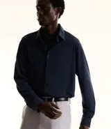 Camisa azul marino de manga larga, confeccionada en tejido piqué de poliamida y elastano. Cuenta con cuello inglés, abotonadura frontal y tecnología performance que ofrece elasticidad, secado rápido y resistencia a las arrugas.