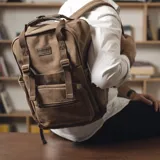 Mochila marrón de tela canvas con compartimento para notebook y accesorios de mate.
