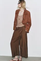 Pantalón cropped marrón de tiro medio y pierna ancha, confeccionado en hilatura con mezcla de lyocell. Presenta trabillas en la cintura, bolsillos laterales y pinzas en el delantero. Cierre frontal con cremallera y botón.