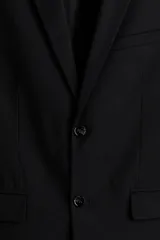 Blazer negro de corte slim fit, con solapas de muesca finas y ojal decorativo. Modelo de botonadura sencilla con bolsillo superior insertado, bolsillos delanteros con solapa, dos bolsillos en el interior y botones decorativos en los puños. Abertura doble atrás.