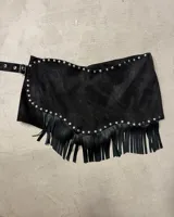 Short pollera negro de efecto gamuza o cuero sintético, con borde festoneado y tachas metálicas plateadas. Presenta flecos largos en el ruedo inferior y se ajusta con una hebilla en el lateral.