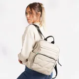 Mochila color beige con diseño acolchado en forma de rombos. Tiene un bolsillo frontal con cierre, dos bolsillos laterales abiertos y un bolsillo interno con cierre. Las correas son ajustables y tiene un asa superior para llevar en la mano.