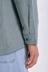 Sobrecamisa verde con rayas verticales blancas, de corte holgado, manga larga, cuello camisero y dos bolsillos frontales con solapa.