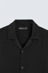 Camisa de calce relajado confeccionada en tejido fluido de mezcla de viscosa, color blanco. Presenta cuello bowling, manga corta, aberturas laterales en el bajo y cierre frontal con botones al tono.