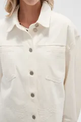 Campera de jean color crudo, de corte recto, con cuello clásico, cierre frontal con botones metálicos, dos bolsillos con solapa en el pecho y bajo con detalle de bordado calado.
