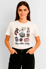 Remera de algodón color crudo con cuello redondo y mangas cortas. Estampado con motivos de comida y la frase "Chic vibes only".