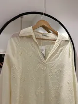 Blusa color crudo con bordados calados, cuello camisero y mangas largas con puño.