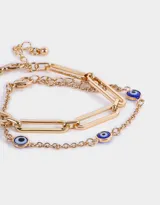 Set de dos pulseras doradas: una de eslabones grandes y otra de cadena fina con dijes de ojo turco.