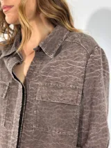Chaqueta color gris con textura, de corte recto, cuello camisero, cierre frontal con botones, mangas 3/4 con puños arremangados, dos bolsillos de parche en el pecho y ruedo recto.