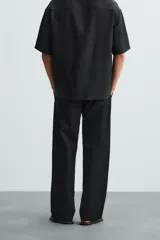 Pantalón negro de corte recto y calce relajado, confeccionado en tejido de algodón con elasticidad. Presenta cintura ajustable con cordón, bolsillos frontales y bolsillos traseros de doble vivo.