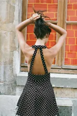 Vestido corto negro con lunares blancos, cuello halter y escote pico. Detalle de lazo en la espalda y cierre lateral con cremallera oculta.