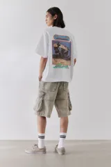 Remera blanca de algodón pesado con cuello redondo ribeteado, hombros caídos, bajo recto y estampado pequeño en el pecho. Corte oversized.