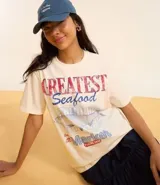 Remera t-shirt de algodón color crema, con cuello redondo y mangas cortas. Estampa frontal con la frase "Greatest Seafood" y un dibujo de un pez.