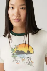 Remera blanca de algodón con cuello redondo ribeteado en verde y estampa de paisaje con sol en tonos naranja, verde y marrón.