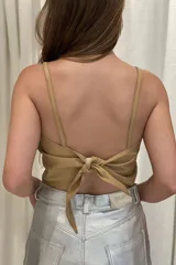 Top corto color crudo, confeccionado en cuero, con breteles finos y espalda descubierta con nudo ajustable.