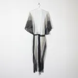 Ruana larga tejida a crochet en degradé de blanco a negro, con mangas murciélago y flecos en el ruedo. Incluye cinturón fino negro para ajustar a la cintura.