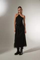 Vestido midi negro de bretel fino, con corte al cuerpo, cuello asimétrico y detalle de nudo en la cintura.